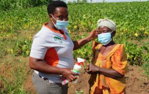 Notre Chargée de Programmes aide une agricultrice à mettre son masque durant une visite de suivi des cultures en Ouganda.