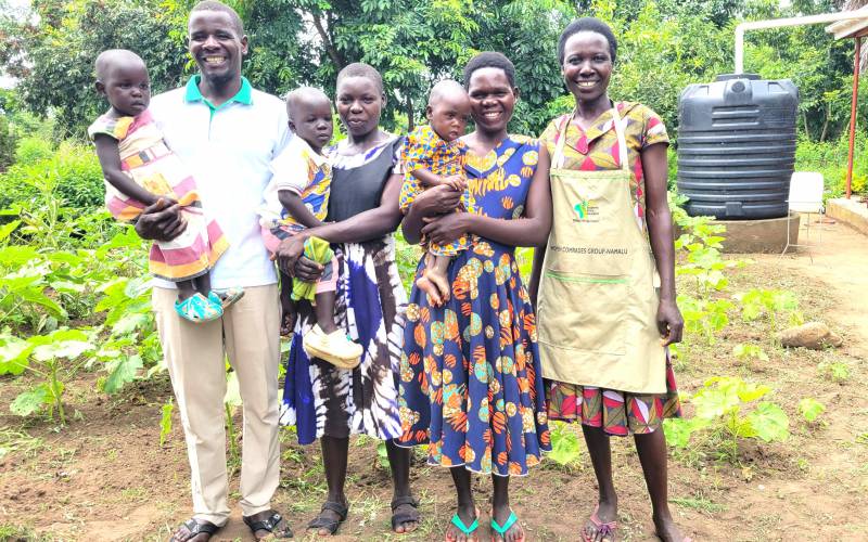From left, Okello Innocent and Nancy, each carrying one of their twins, pose for a photo with members of the Nutrition Model Home in Kole District.