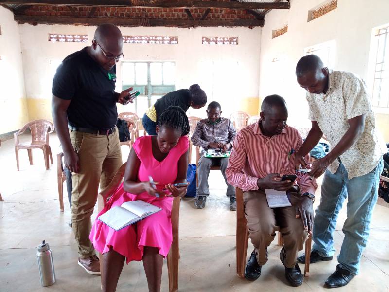 キボガ地区にて、農業普及員とm-Omulimisaのスタッフがアプリの使い方を指導している様子